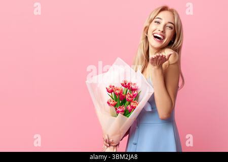 Giovane donna allegra con fiori di primavera bella ridere e guardare a fotocamera su sfondo rosa studio Foto Stock