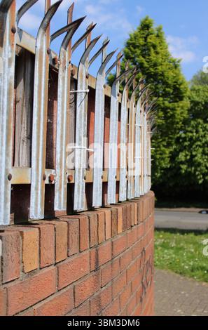 Muro di pace in mattoni dell'epoca dei problemi con punte metalliche appuntite e piegate in cima nel quartiere Shankill Road di Belfast, Irlanda del Nord Foto Stock