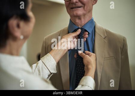 Donna che regola con cura la cravatta da uomo anziano in un elegante abbigliamento da lavoro, creando un look professionale e raffinato. La vista ravvicinata cattura i momenti più intimi e i dettagli precisi Foto Stock