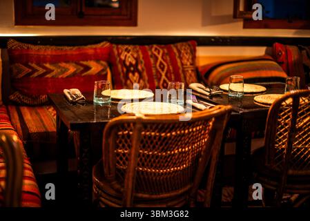 Tavolo per due con cuscini marocchini e sedie in vimini all'interno di un locale storico di Marrakech Foto Stock