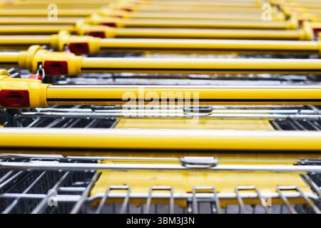 Carrelli gialli in fila. Vista superiore astratta dei quadratini di ridimensionamento. Dettaglio del mercato retail. Primo piano delle maniglie del carrello. Sfondo modello commerciale. Foto Stock