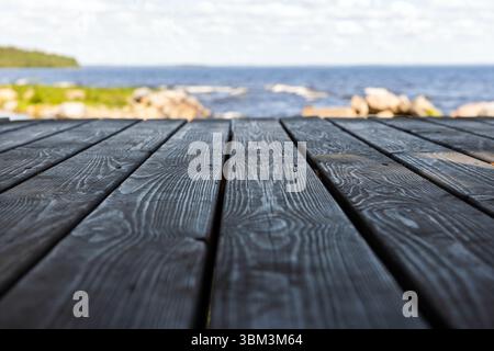 Vista grandangolare di un ponte in legno in primo piano su una sponda panoramica sfocata con acqua blu. Sfondo podio vuoto con messa a fuoco morbida selettiva Foto Stock