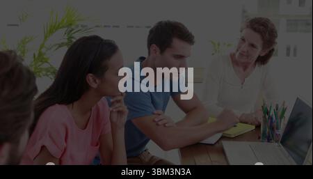 Brainstorming di quattro colleghi utilizzando un computer portatile e un blocco note giallo nella sala riunioni, con matite colorate Foto Stock