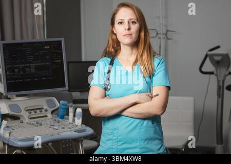 Ritratto di donna medico o ecografo in scrub in piedi nella moderna sala diagnostica a ultrasuoni con attrezzature mediche e stetoscopio Foto Stock