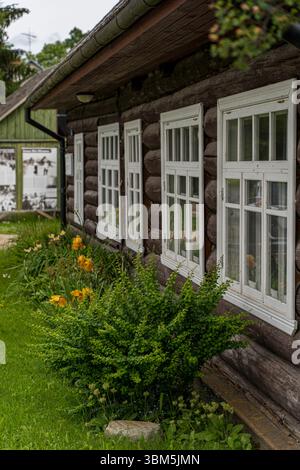 Tradizionale casa in legno con finestre incorniciate di bianco e giardino fiorito a Obinitsa, Setomaa, Estonia Foto Stock