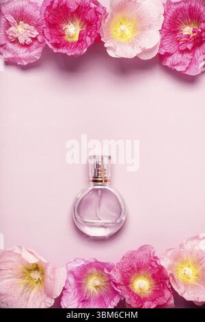 Le donne della bottiglia di profumo e di rosa fiori di malva su sfondo rosa. Il minimalismo Il concetto di bellezza Foto Stock