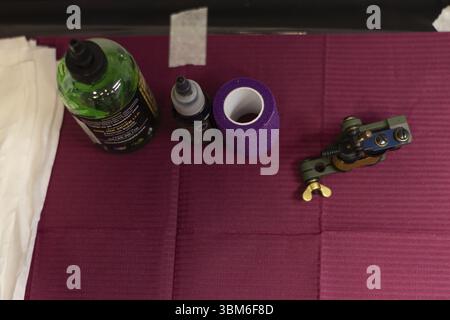 Tavolo di un tatuatore con strumenti per tatuaggi, macchina per tatuaggi, nastro viola, inchiostro e vaselina Foto Stock