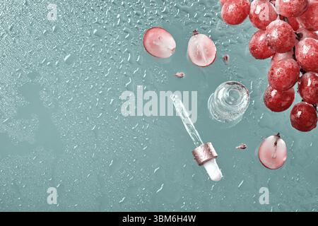 Cosmetici biologici con olio di semi d'uva e ingredienti a base di erbe. Zero sprechi di vino. Bottiglia di prodotto per la cura della pelle, uva e gocce d'acqua su sfondo blu Foto Stock