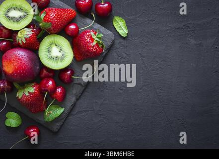 Mix di succosa frutta estiva e bacche. Fragola, ciliegia, kiwi e pesche su nero ardesia piastra. Vista da sopra con lo spazio di copia Foto Stock