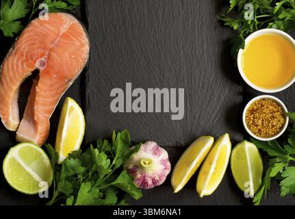 Crudo fresco bistecca di salmone e gli ingredienti per la preparazione intorno al bordo di taglio. Vista da sopra con lo spazio di copia Foto Stock