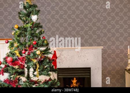 L'albero di Natale decorato si trova in un angolo piatto di design, con baule e calze rosse Foto Stock