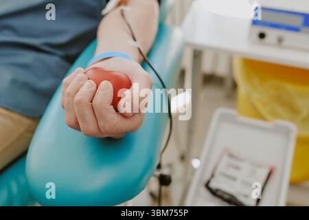 Uomo di mezza età caucasico che donava sangue e spremeva stress Ball alla clinica Foto Stock