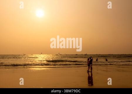 Un romantico tramonto dorato illumina il cielo a Baga Beach a Goa, India, mentre una coppia cattura un gioioso selfie sulla costa. Foto Stock