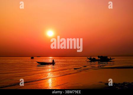 Uno splendido tramonto dorato illumina il fiume Padma a Moinot Ghat vicino a Dacca, Bangladesh, dove le barche tradizionali riposano dolcemente sull'acqua. Foto Stock