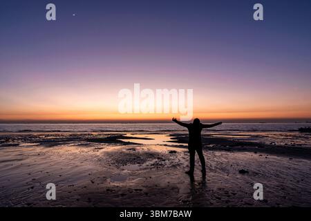 Una vista serena del tramonto su una spiaggia di Chattogram, Bangladesh. L'orizzonte arancione luminoso incontra il mare calmo, con riflessi delicati. Foto Stock