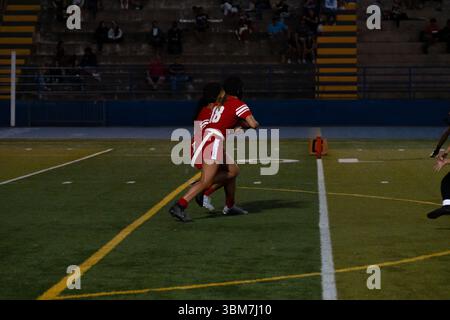 Titolo: Ragazze in uniforme rossa che giocano a flag football in un vivace spettacolo sul campo lavoro di squadra, energia, empowerment negli sport giovanili, temi atletici del lavoro di squadra Foto Stock
