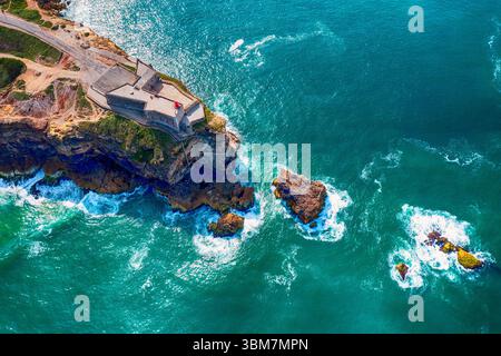 Rocky Cape con un faro nella città di Nazare in Portogallo sulle rive dell'Oceano Atlantico Foto Stock