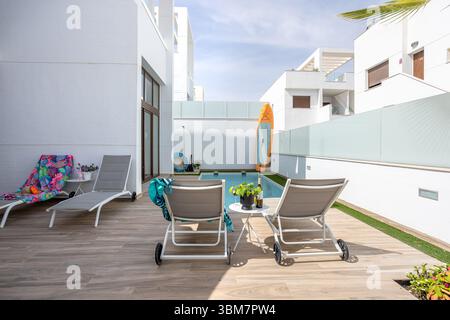Piscina al piano terra con lettini, paddle board e area salotto ombreggiata in un cortile pulito. Foto Stock