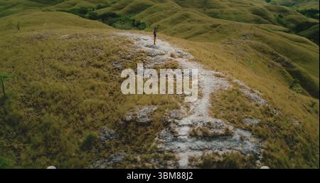 Vista aerea delle colline e delle valli verdi ondulate con un turista in piedi sulla cima di una collina che ammira la vista mozzafiato dell'isola di Sumba, Indonesia Foto Stock