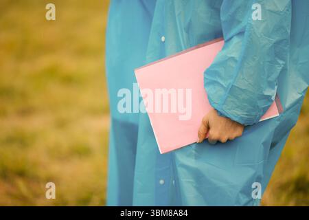 Persona in impermeabile con una cartellina rosa ricoperta di gocce di pioggia. Colori brillanti e texture bagnata Foto Stock
