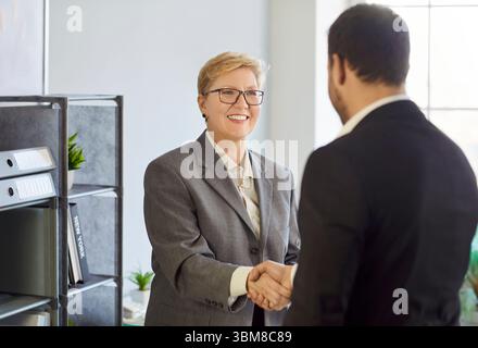Donna e uomo che stringono la mano, sorridono suggerendo nuove interazioni positive, saluto, accordo Foto Stock