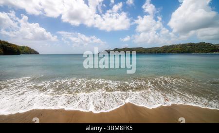 Onde dolci si infrangono sulla spiaggia sabbiosa di Kings Bay, acque cristalline turchesi, il vasto orizzonte e le morbide nuvole creano un tranquillo e incontaminato trop Foto Stock