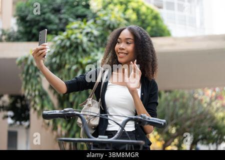 Selfie e spirito ciclistico. Giovane donna che si fa un selfie accanto alla sua bicicletta, piena di gioia ed eccitazione. Foto Stock