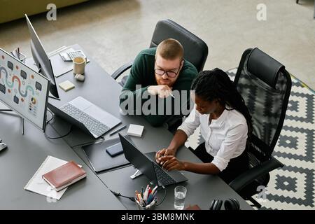 Scoprire i dettagli durante la collaborazione sul progetto in un ambiente di lavoro moderno. Colleghi eterogenei impegnati in discussioni, interagendo con i dispositivi digitali e condividendo idee Foto Stock