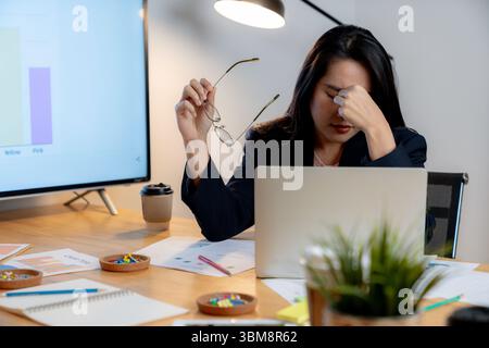 Donna stanca che lavora in ufficio si sente affaticata dagli occhi dopo aver lavorato fino a tardi davanti a un computer. Foto Stock
