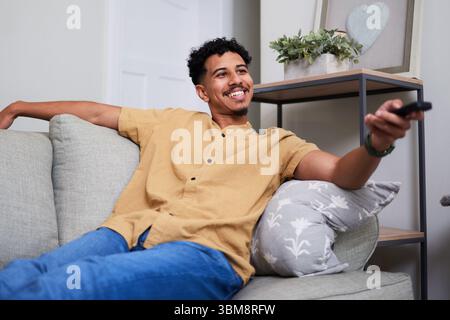 Giovane uomo che si gode momenti rilassanti guardando la televisione a casa nel confortevole spazio abitativo Foto Stock