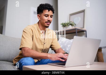 Giovane concentrato che lavora sul suo notebook a casa su un comodo divano Foto Stock
