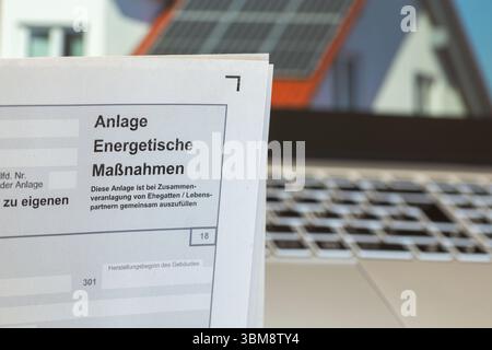 Primo piano della dichiarazione dei redditi, allegato misure energetiche, sullo sfondo un'immagine di un tetto solare sullo schermo di un notebook Foto Stock