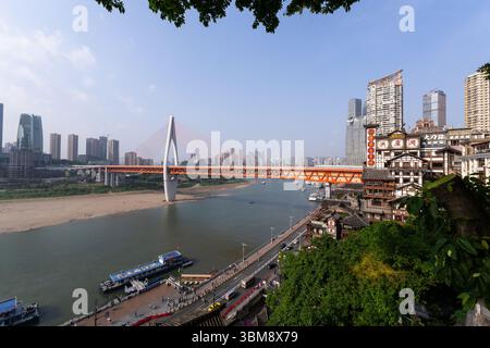 Chongqing, Cina - 10 maggio 2025: Il ponte Qiansimen attraversa il fiume Yangtze a Chongqing con la famosa area panoramica della grotta di Hongya in Cina Foto Stock