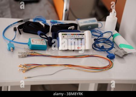 Configurazione della polisomnografia per lo studio del sonno: Monitor ECG, cavi, elettrodi, tavolo bianco, apparecchiatura diagnostica sanitaria, scena clinica Foto Stock