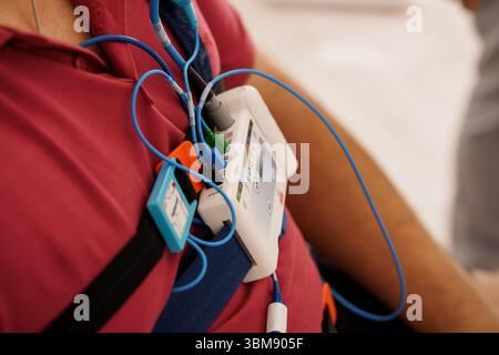 Primo piano del sistema di polisomnografia portatile per il monitoraggio della schiena del paziente, dei fili blu, dei dispositivi medici, dello studio clinico del sonno, della maglia rossa. Foto Stock