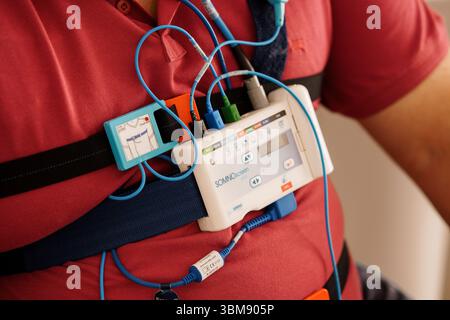 Diagnosi dell'apnea nel sonno con dispositivo PSG portatile sulla schiena del paziente. Camicia rossa, apparecchiature di monitoraggio, ambiente clinico, tecnologia sanitaria, diagnostica Foto Stock