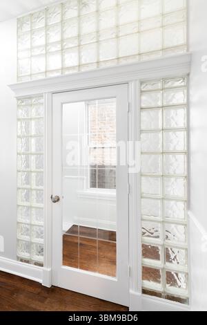 Una porta frontale interna con pareti bianche, finestre a blocchi di vetro, pavimenti in legno scuro e una grande finestra sulla porta. Foto Stock