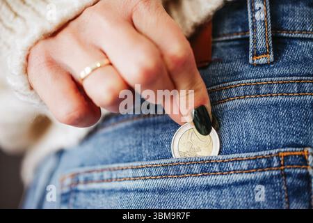 Donna che mette la moneta nella tasca dei jeans. Risparmio di denaro e concetto di finanza personale. Budget giornaliero e controllo del reddito. Contanti in mano per piccole spese. Foto Stock