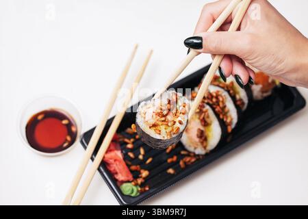 Donna che usa le bacchette per scegliere il sushi roll. Cucina giapponese servita con salsa di soia. Elegante presentazione dei pasti su sfondo bianco. Momento gustoso del cibo. Foto Stock