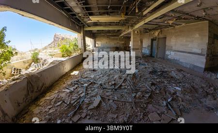 L'interno di un edificio abbandonato, distrutto dalla guerra, con detriti e pareti rotte, luce solare che scorre attraverso grandi finestre, creando un contrasto tra decadimento e na Foto Stock