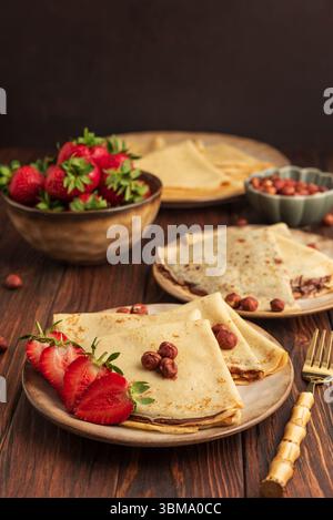 Crepes con crema di nocciole al cioccolato, fragole e nocciole su un tavolo di legno. Foto Stock