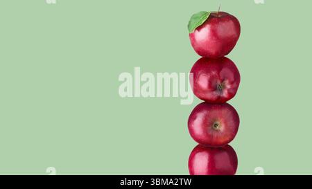 Mele rosse impilate una sopra l'altra sullo sfondo color salvia. Equilibrio Foto Stock