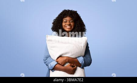 Giocosa donna nera che abbruttava un grande cuscino sul giallo Foto Stock