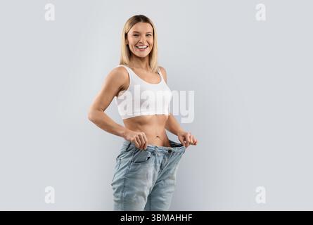 Donna felice di mezza età che indossa jeans grandi dopo la perdita di peso Foto Stock