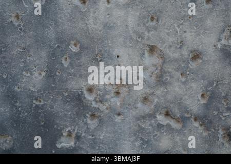Una fotografia astratta da vicino di una superficie grigia pesantemente segnata da buchi di proiettili e schegge della seconda guerra mondiale a Berlino, in Germania. Foto Stock
