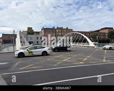James Joyce Bridge a Dublino, Irlanda, noto come ponte a libro aperto. Moderno ponte pedonale sul fiume con edifici cittadini e auto. Foto Stock