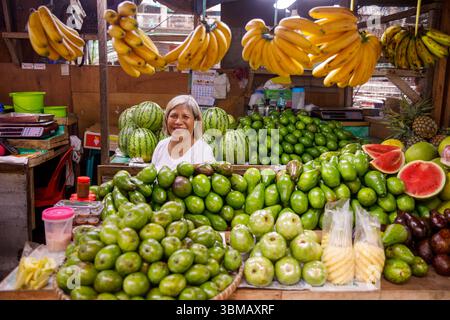 13 maggio 2025: Calapan City, Filippine, venditore femminile sorridente che vende banane angurie avocado e altri frutti tropicali al mercato pubblico Foto Stock