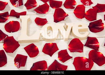 Il segno d'amore viene mostrato in una composizione piatta su una tavola di legno bianca con petali di rosa rossi Foto Stock