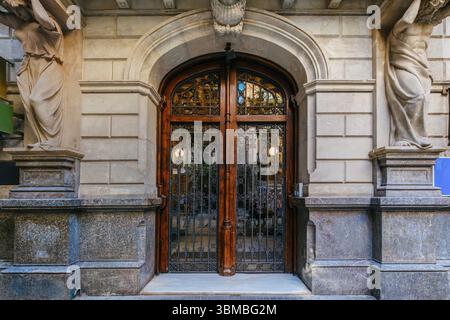Una porta d'ingresso in legno splendidamente lavorata con dettagli intricati e una figura in pietra scolpita sopra, in un classico edificio di Barcellona. Mostra i ricchi Foto Stock