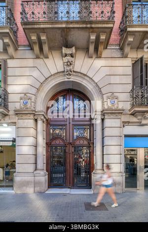 Ingresso al suggestivo edificio di Barcellona con porta in legno ornamentale e arco, passeggiata con persona sfocata. Architettura classica spagnola, scena urbana, Foto Stock
